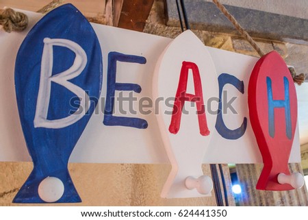 Wooden beach sign with fish hanging on rope in red blue and white
