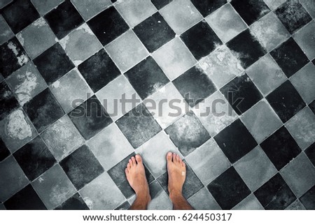 Close up of barefoot man's feet at mosaic aged damaged ceramic tiles floor. Conceptual photo. Point of view.