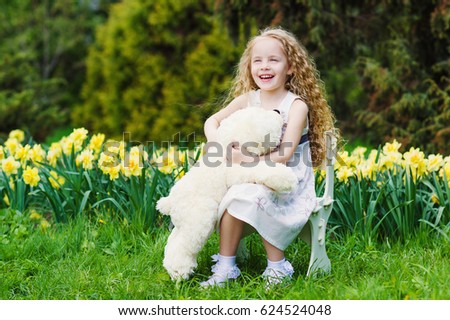 Happy little girl with her bear toy in blooming garden
