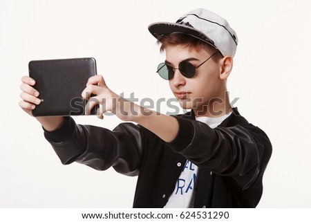 Studio shot of trendy teen in a cap and sunglasses and holding a tablet isolated on white background