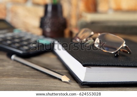 The diary, glasses and a simple black pencil lie on the desktop. Close-up. Selective focus