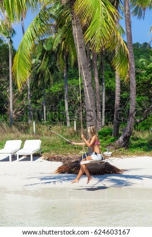 Attractive blond girl making selfie with action camera sitting on a swing on a luxury tropical beach, with white sand, turquoise water, blue sky. Paradise island Phu Quoc, Vietnam, Bai Sao. Copy space