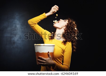 Attractive young woman pouring popcorn in mouth holding big bucket