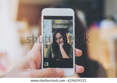 A man using white smart phone taking a picture of a beautiful woman in wooden vintage cafe