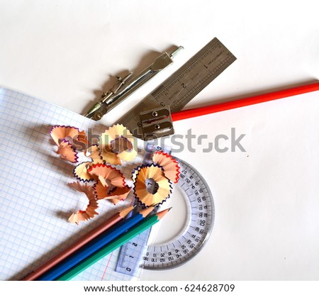 cell school notebook on which there are sharp colored pencils, pencil sharpener, compasses, ruler, protractor and sawdust isolated