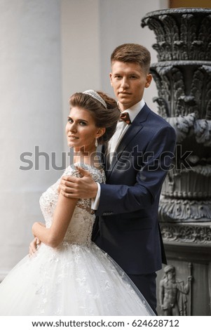Groom holds bride's shoulders standing before tall black vase