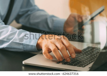 close up of businessman working with mobile phone and laptop computer  on wooden desk in modern office 