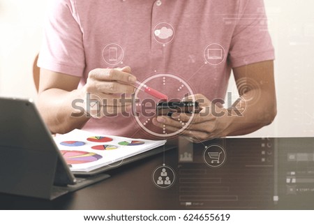 businessman in pink t-shirt working with smartphone and digital tablet computer and document on wooden desk in modern office with virtual icon diagram