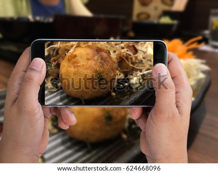 man holding smartphone taken Takoyaki; Japanese food photo on the table to share social network