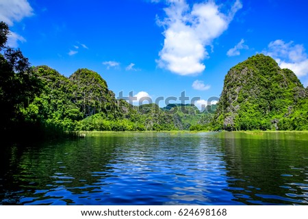 Tourists traveling in boat along the Ngo Dong River taking picture of the Tam Coc, Ninh Binh, Vietnam. Rower using her feet to propel oars. Landscape formed by karst towers and rice fields in Vietnam
