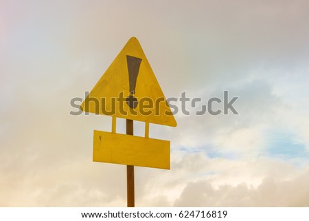 Exclamation point of attention on a yellow triangular sign with a sign for signing. Against the sky in the sunset. Warning, danger.