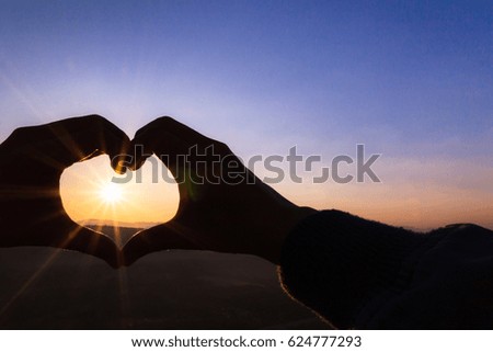Sun in heart shape hands; Silhouette of couple hand holding sun rays with mountain in sunrise scene (copy space for text)