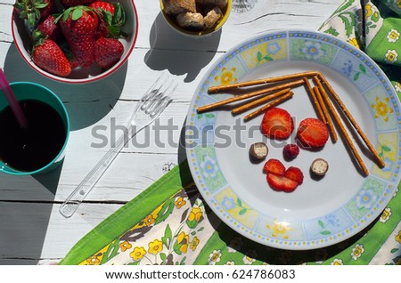 Snack time: creative strawberry in the form of a cute woman face, bowl with strawberries and cashew nuts on white wooden background (top view)