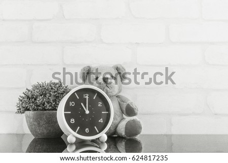 Closeup alarm clock for decorate in 11 o'clock with bear doll and plant on black glass table and white brick wall textured background in black and white tone with copy space