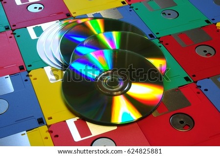 Old diskette 5 25 inches with 3.5 floppy disks of various colors with modern DVD. Background