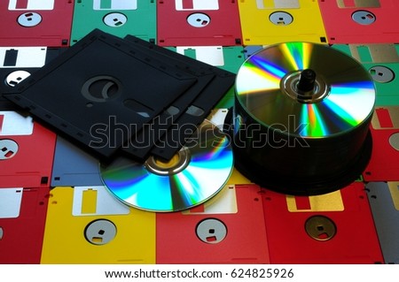 Old diskette 5 25 inches with 3.5 floppy disks of various colors with modern DVD. Background