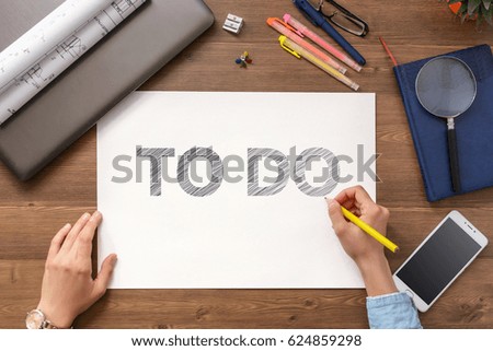 The girl sits at the table with a mobile phone, a laptop, business accessories and a sheet with text To do