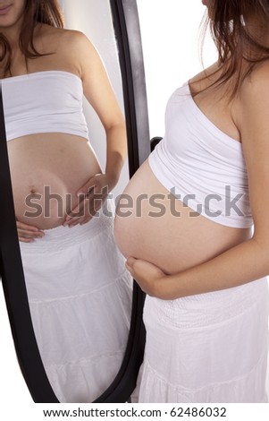 A mom is pregnant holding her belly by a mirror.