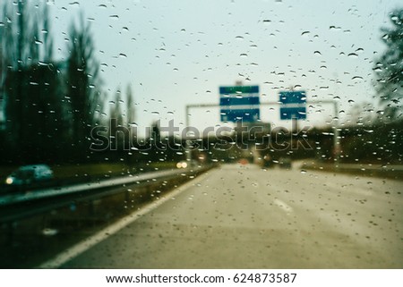 Personal perspective of driver inside car looking at the front view of the highway autobahn on a heavy rain trying to read the defocused highway sign