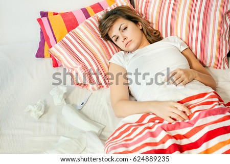 Sick young woman lying in bed. She has cold and flu. 