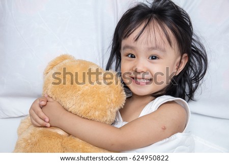 Asian little Chinese girl hugging a teddy bear on the bed at home