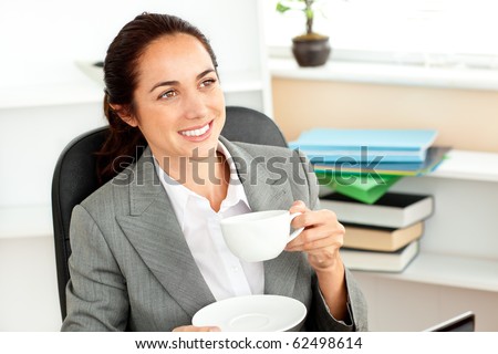 Cheerful hispanic businesswoman drinking coffee at her desk in her office
