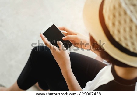 young woman holding a black screen of smart phone, playing a social media, sitting in a public park