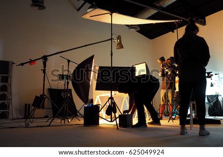 Silhouette of people working in production studio for shooting or recording by digital camera and lighting set.