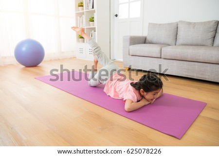 kid having fun doing some morning gymnastic with fitness stretching at home lying down on the floor with mat in the living room. family activity and healthy lifestyle concept.