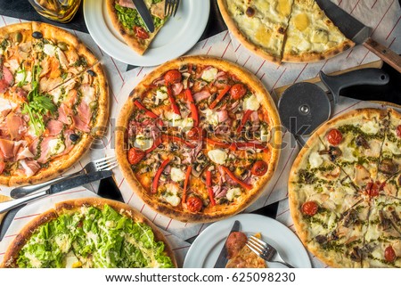 Pizza on paper on a wooden board and pieces of pizza in plates. A lot of pizza on a black table close up. Healthy hot food. Royalty-Free Stock Photo #625098230