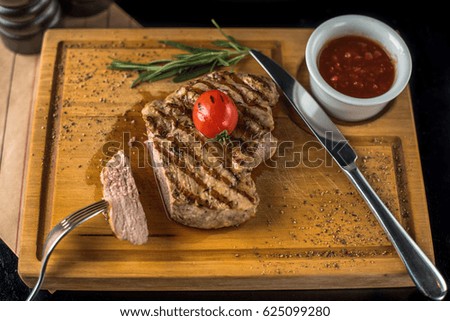 Steak and tomato sauce on a wooden board. Grilled meat on a black background close-up. Healthy hot food.