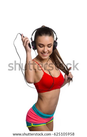 Happy female athlete at gym. Dressed in bra in panties she dancing to favorite music using headphones. Beauty of female slim and strong body, isolated on white.