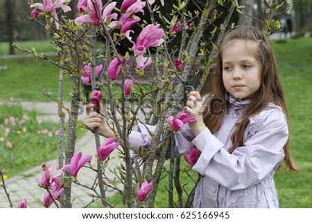 Girl in purple cloak and with long hair next to a blooming Magnolia tree
