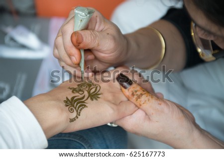 Henna Artist applying henna tatoo on woman's hand.