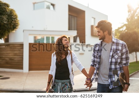 Portrait of a smiling young couple holding hands and carrying skateboards.