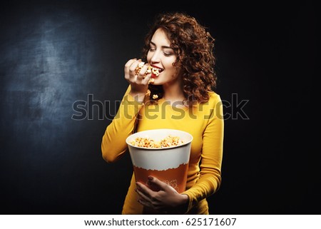 Hungry woman eats handful of popcorn while waiting for movie