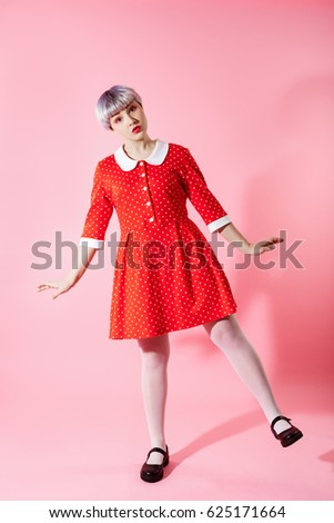 Picture of beautiful dollish girl with short light violet hair wearing red dress over pink background.