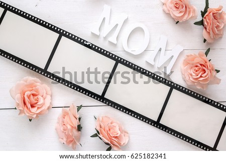 Background with a frame in the form of a film, pink roses and mothers day message on white wooden table. Space for text or image. 