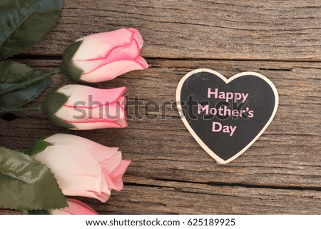 Happy mother's day writing on a heart shape tag with flowers over wooden background