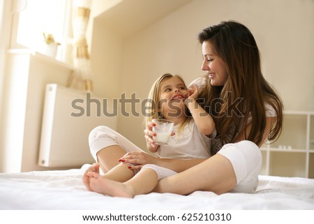 Mother with her cute little daughter sitting on bed. 
Enjoy together in free time. Royalty-Free Stock Photo #625210310