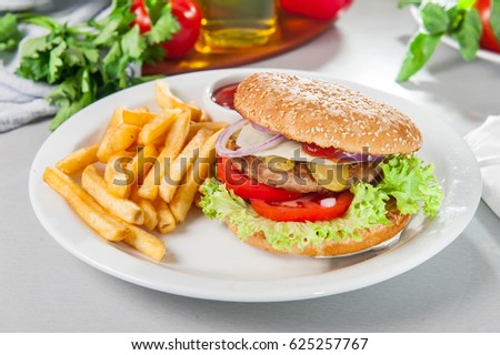 Tasty burger set - meat burger, french fries and sause on the white round plate on the served table with fresh ingridients. Close- up. selective focus. Unhealthy food concept