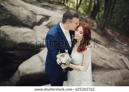 Tender kiss of bride and groom standing on the stones in the forest