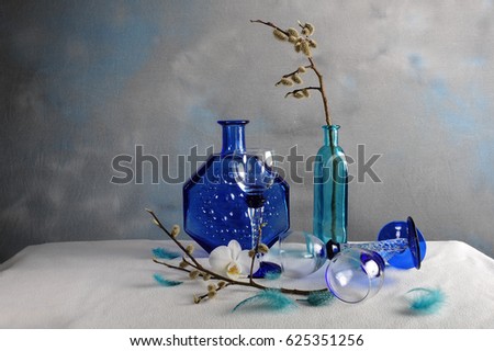 Beautiful still life of blue an turquoise vases, liqueur glasses and catkins, feathers and one single white orchid. Copy space to the left in horizontal photo.