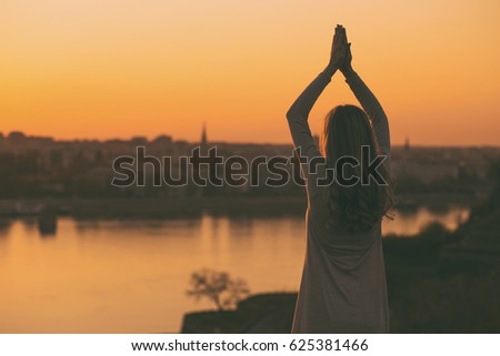 Silhouette of a female meditating at the sunset.Woman relaxing outdoor
Image is intentionally toned.