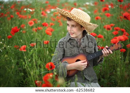 young boy wearing a hat, playing guitar on a meadow with poppies, in summer