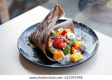 Crispy crepe with colorful mixed fruit, mango, banana, strawberry, dragon fruit and  kiwi topped over with vanilla ice cream, icing, raspberry sauce and sliced roasted almond.