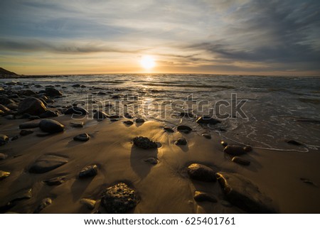 Beautiful golden sunset at north sea. Amazing sea picture background. Sunset splash water waves. Beach with sand and rocks. Summer time. Vacation concept.