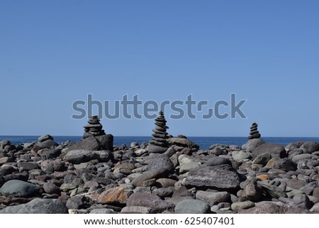 In the picture are pebbles, some of them are placed to three pyramids. In the background is the blue clear sky. Sun is shining. It's very harmonic photo. The second pyramid is in the center.