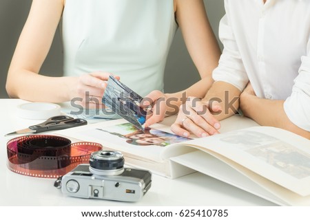 Making young family photo album. Newly married or engaged couple looks and chooses printed pictures to glue them into wedding album