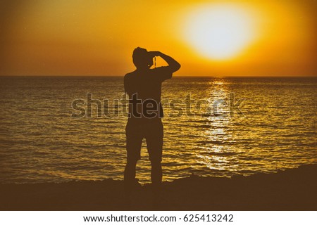 Retro image of silhouette of a man taking a photo of sunset over the Mediterranean Ocean